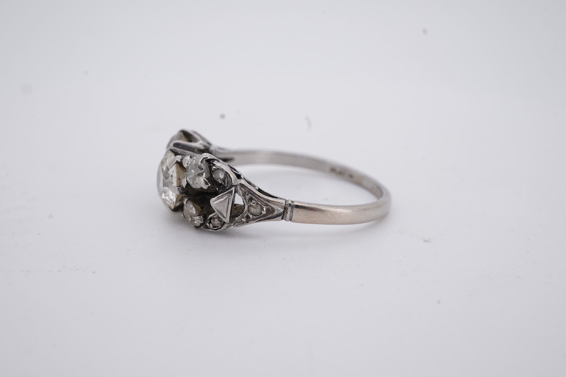 A white metal (stamped platin) and single stone diamond ring, flanked by four smaller diamonds and rose cut diamond chip set shoulders, size P, gross weight 3.8 grams.